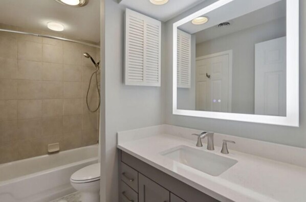 A modern bathroom with a bathtub, toilet, and a large mirror above the sink. - Completely Updated Two Bedroom Villa with Large Open Concept! (Hilton Head)