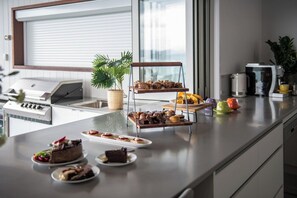 A modern kitchen with a countertop displaying various pastries and a coffee machine. - The View (Airlie Beach)