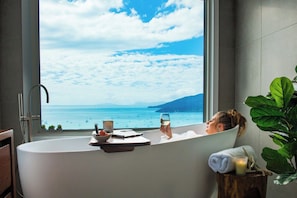 A bathtub with a view of the sea, a window, and a plant.