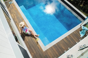 A swimming pool with a wooden deck, a person sitting by the pool, and a towel on the deck.
