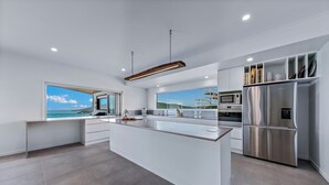 A modern kitchen with a large island, stainless steel appliances, and a view of the sea. - The View (Airlie Beach)