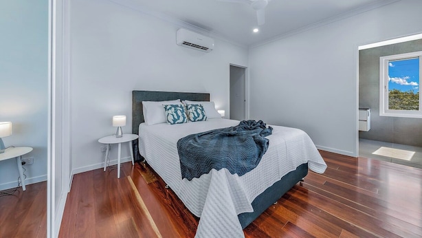 A modern bedroom with a bed, bedside tables, a ceiling fan, and an air conditioning unit. - The View (Airlie Beach)