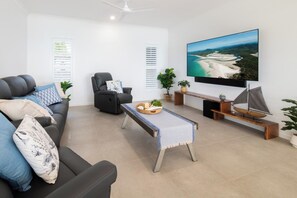 Un salon moderne comprenant un canapé, un fauteuil, une table basse et un téléviseur diffusant un paysage pittoresque.