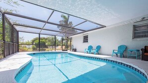 Ein Swimmingpool mit Glasveranda, umgeben von blauen Stühlen und Blick ins Grüne.