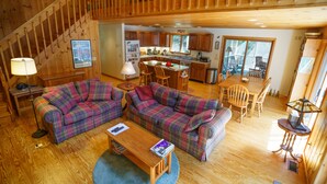 A cozy cabin interior with plaid sofas, a wooden dining table, and a kitchen area.