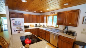 A kitchen with wooden cabinets, a stainless steel dishwasher, a red kettle, and a microwave.