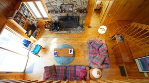 Cozy cabin-style room with a stone fireplace, comfortable seating area, and a bookshelf filled with books.