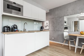 Uma cozinha moderna com armários brancos, forno de aço inoxidável e cafeteira na bancada.