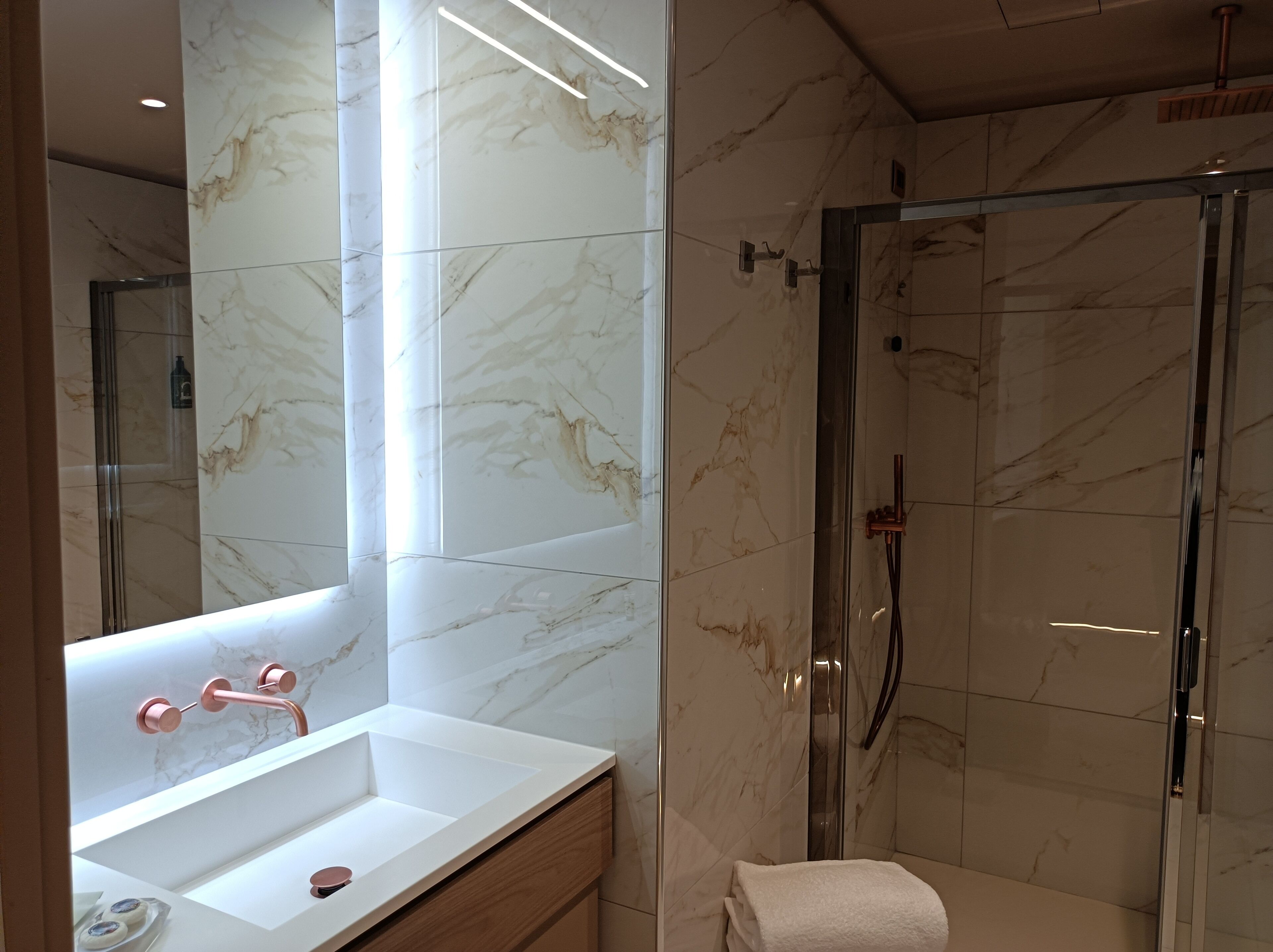 Un baño moderno con tocador de mármol, cabina de ducha de vidrio y un espejo grande.