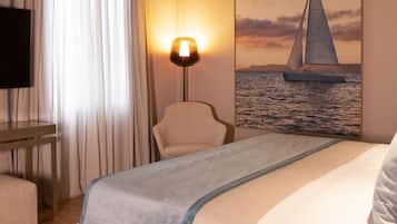 Habitación de hotel con cama, una silla, un escritorio, una lámpara y un cuadro de un velero en la pared.