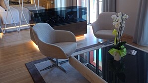 A modern hotel room with a glass coffee table, two armchairs, a sofa, a TV, and a large window with curtains. - Miramare Suites (Sestri Levante)