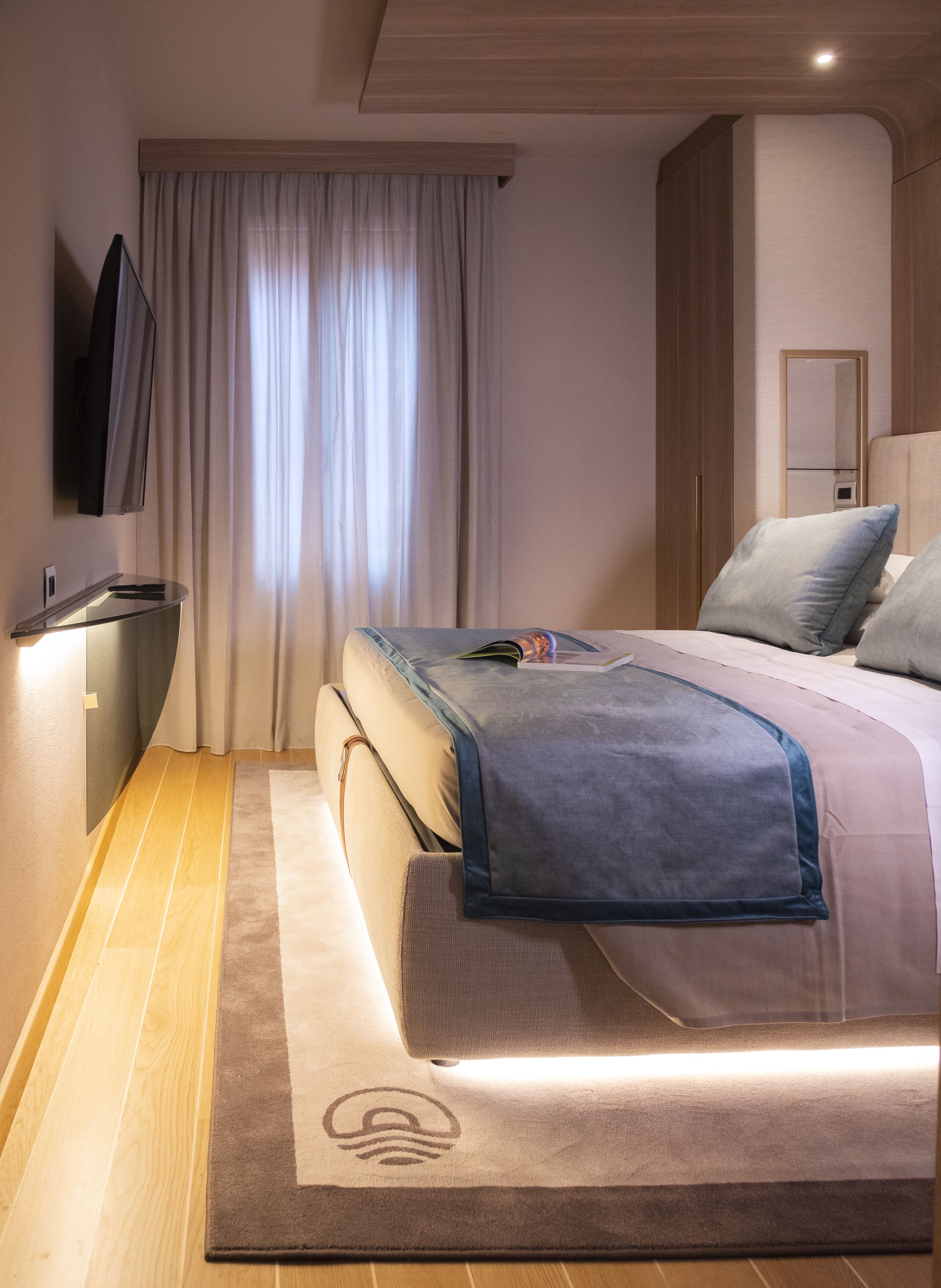 Una camera d'albergo moderna con un letto, una televisione a schermo piatto, una scrivania e un'ampia finestra con tende.