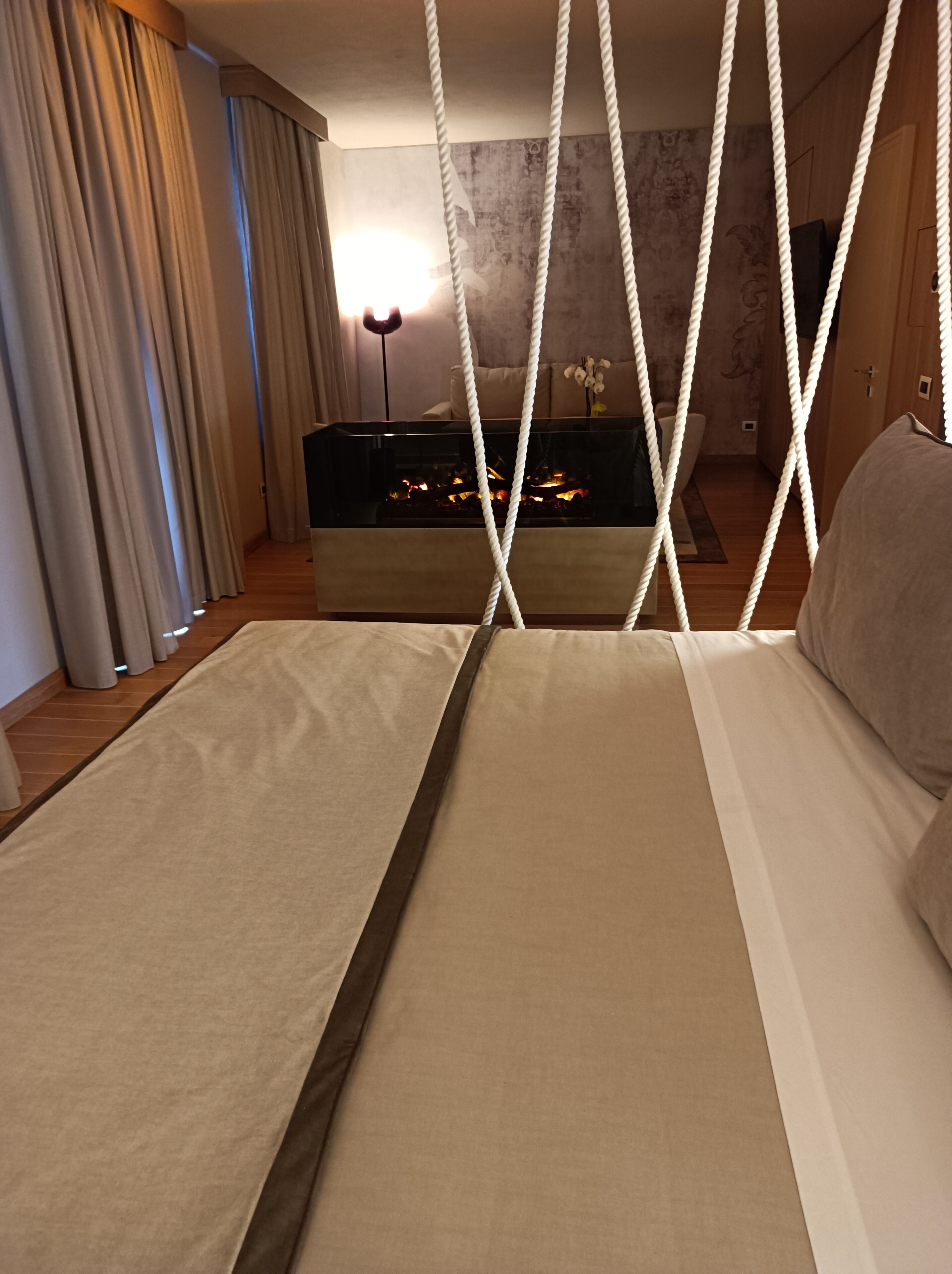 A modern hotel room with a large bed, a fireplace, and a view of the cityscape.