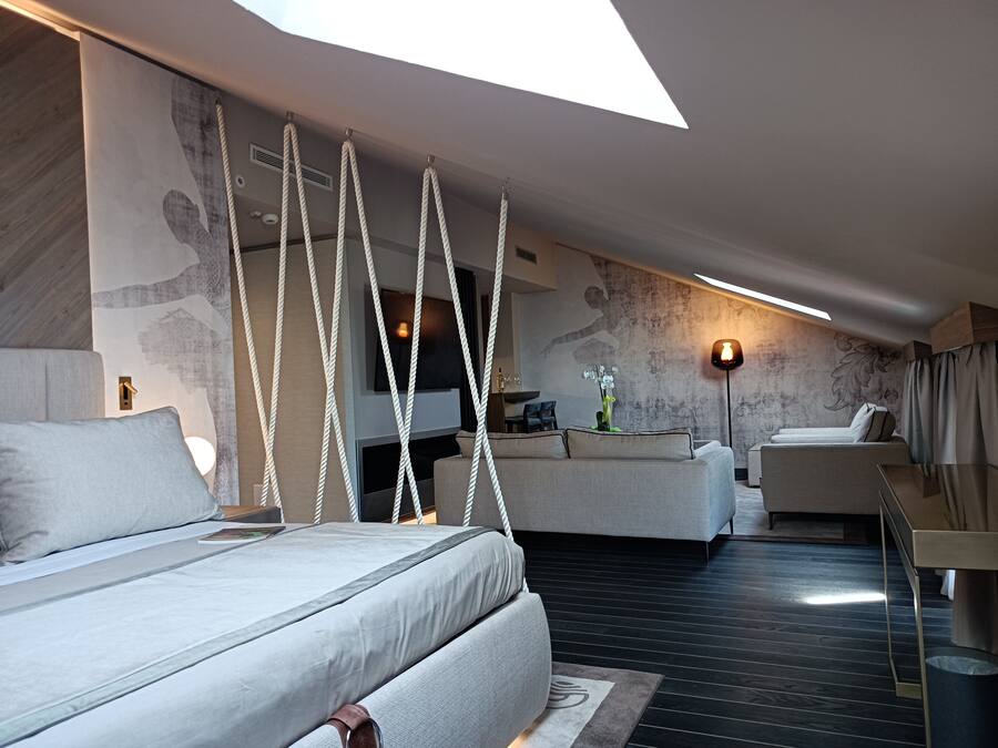 A modern hotel room with a large bed, a sofa, a desk, and a dining area.
