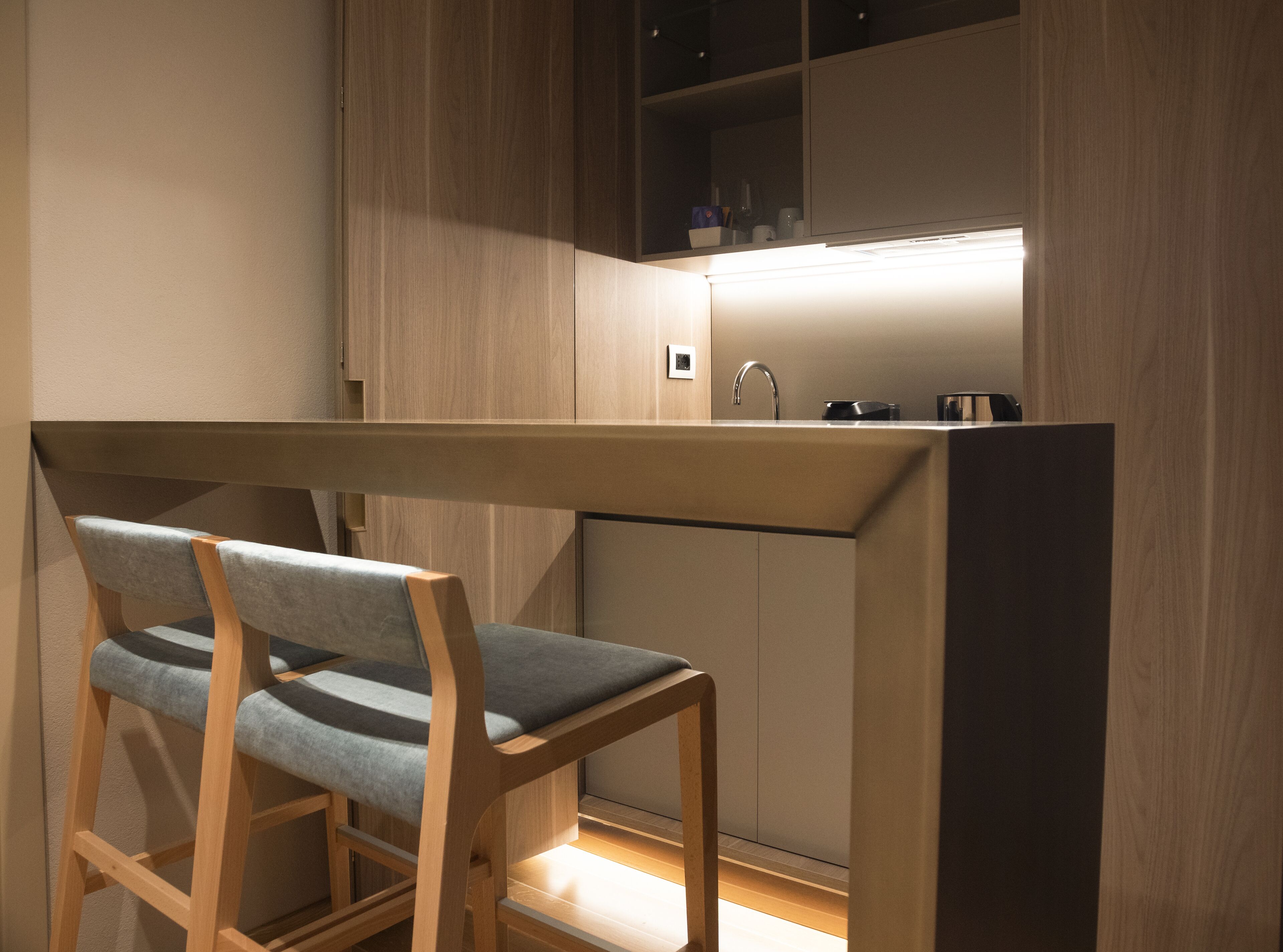 Una cocina compacta con un lavamanos integrado, muebles de madera y un banco con cojines grises.