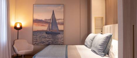 A modern hotel room with a bed, a chair, a painting of a sailboat, and a lamp.