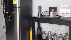 A kitchen with a stainless steel refrigerator, a black table with a coffee machine, and a shelf with kitchenware. - Casa Ines Hostal a place especially for you... (Santa Marta)