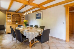 A dining area with a round table set for six, surrounded by black chairs. There is a wooden cabinet with glass doors to the left, and a painting on the wall above the table.