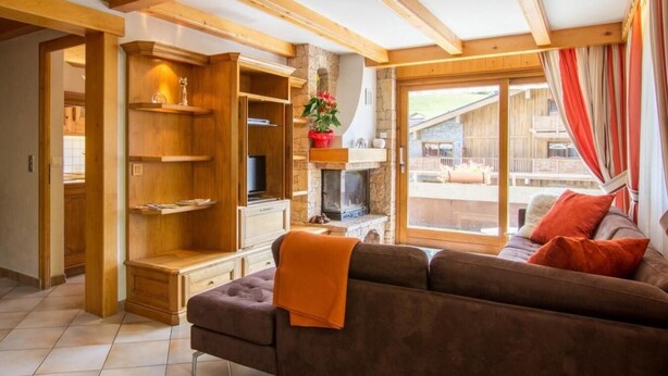 A cozy living room with a sofa, wooden shelves, a fireplace, and a large window with curtains. - 100m from resort center, 1st floor, view mountain/street/ski slopes, terrace, fireplace or stove (Le Grand-Bornand)
