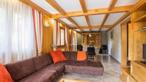 A modern living room with a sectional sofa, wooden beams, a dining area, and a TV on a wooden cabinet. - 100m from resort center, 1st floor, view mountain/street/ski slopes, terrace, fireplace or stove (Le Grand-Bornand)