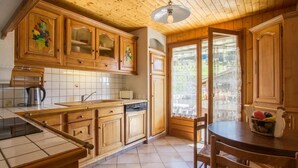 A kitchen with wooden cabinets, a sink, a stove, and a dining area with a table and chairs. - 100m from resort center, 1st floor, view mountain/street/ski slopes, terrace, fireplace or stove (Le Grand-Bornand)