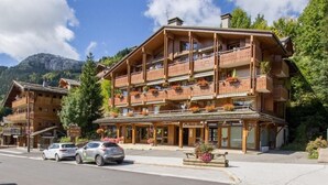 A multi-story wooden building with balconies, a sign for 'Mont-Reve', and cars parked in front. - 100m from resort center, 1st floor, view mountain/street/ski slopes, terrace, fireplace or stove (Le Grand-Bornand)
