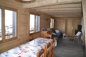 A wooden cabin with a dining table set for four, a sofa, a TV, and a small table with a basket.
