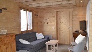 Et hyggeligt sommerhusinteriør med en grå sofa, et lille træbord og en grå stol.