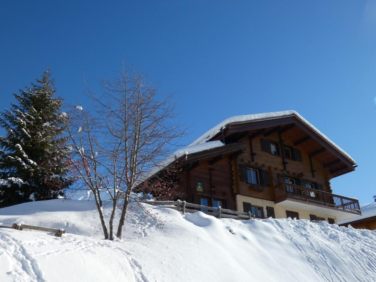 Eine Holzhütte mit Balkon, umgeben von verschneitem Gelände und Bäumen.
