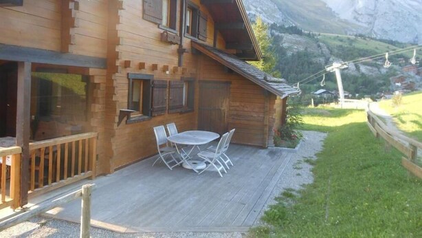 En træchalet med terrasse, udendørs siddepladser og udsigt til et bjerg.