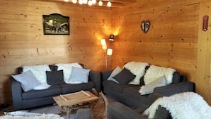 Un acogedor interior de cabaña de madera con dos sofás y una pequeña mesa de madera, una lámpara de pared y un cuadro enmarcado.