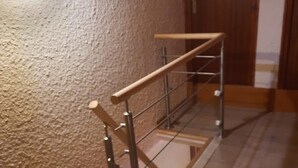 Eine Treppe mit einem hölzernen Geländer und Metallspindeln, die zu einer Holztür führt.