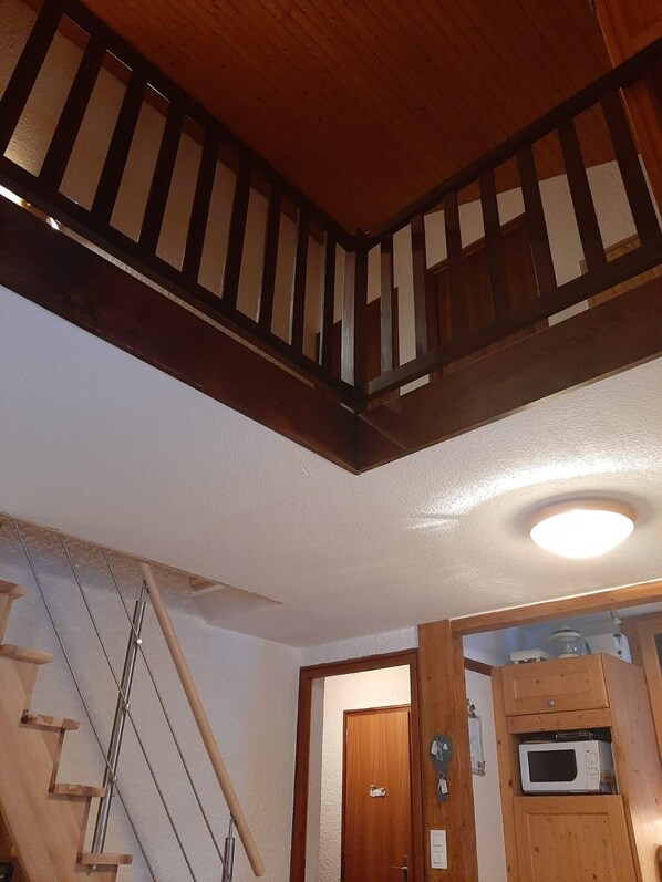 A wooden staircase with a handrail, a white ceiling, and a wooden door with a microwave above it.