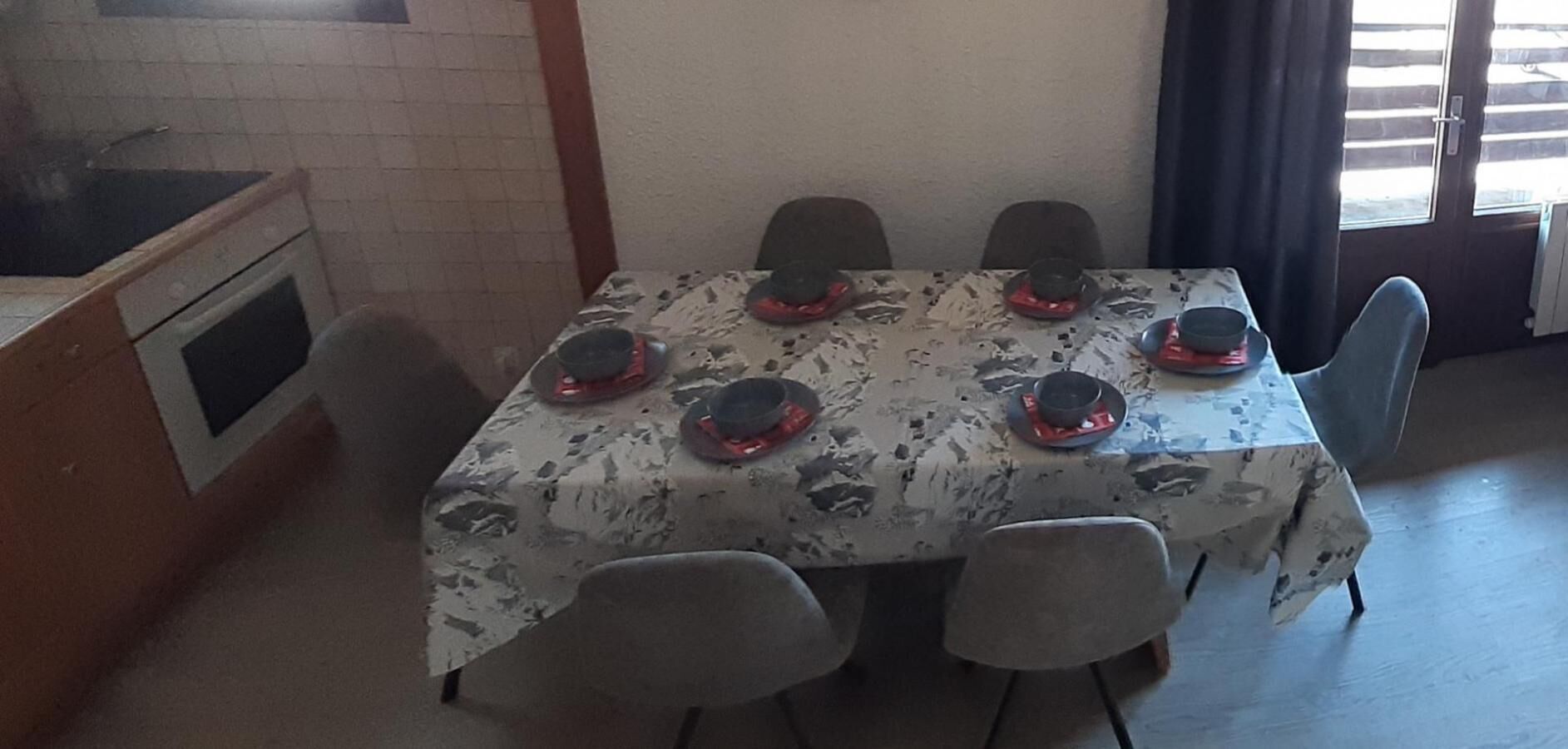 A dining table with four chairs, a tiled backsplash, and a window with curtains.