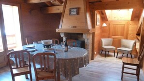 A cozy wooden dining area with a round table and chairs, a fireplace, and a sloped ceiling.