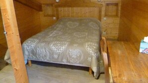 A wooden cabin room with a bed, a wooden table, and a bench.