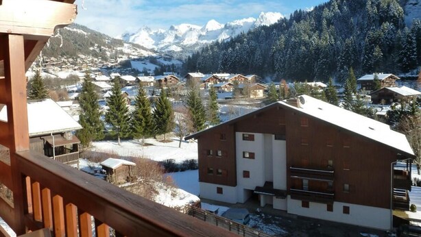 A wooden building with a sloped roof, surrounded by snow-covered trees and mountains in the background.
