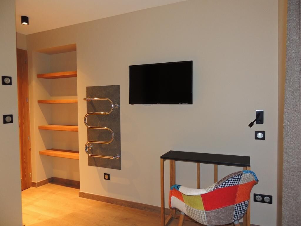A modern room with a wooden floor, a black TV mounted on the wall, and a colorful chair with a woven seat.