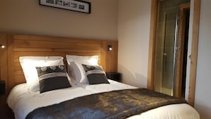 A neatly made bed with a wooden headboard, two bedside tables with lamps, and a framed picture above the bed. - Wifi, 2nd floor, view street/mountain/village, fitness, sauna, balcony, tv, ski locker, 77m² (Le Grand-Bornand)