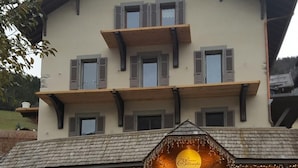 A multi-story building with a stone facade and a wooden upper floor. - Wifi, 2nd floor, view street/mountain/village, fitness, sauna, balcony, tv, ski locker, 77m² (Le Grand-Bornand)