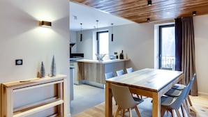 A modern kitchen with a wooden ceiling, a dining area with a large table and chairs, and a view of the city through the window. - Wifi, 2nd floor, view street/mountain/village, fitness, sauna, balcony, tv, ski locker, 77m² (Le Grand-Bornand)