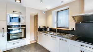 A modern kitchen with stainless steel appliances, a black countertop, and white cabinetry. - Wifi, 2nd floor, view street/mountain/village, fitness, sauna, balcony, tv, ski locker, 77m² (Le Grand-Bornand)