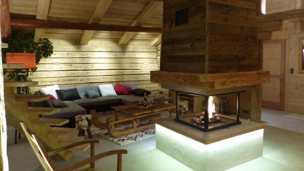 Interior acogedor de una cabaña con techo de madera, chimenea, sofá y mesa de comedor.