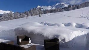 Espacio exterior cubierto de nieve con mobiliario de mimbre y un muro de nieve.