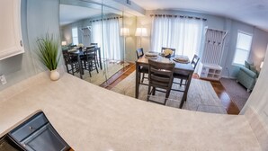 A modern kitchen with a dining area, a large mirror, and a view of the living room. - Top Rated! Beautifully Updated Bayside Condo with Pool! (Ocean City)