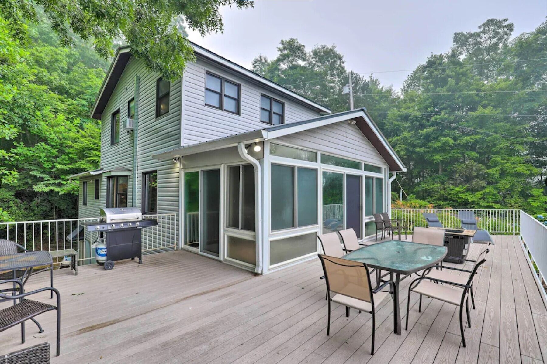 A house with a covered patio area featuring a table and chairs, a grill, and a trash can.