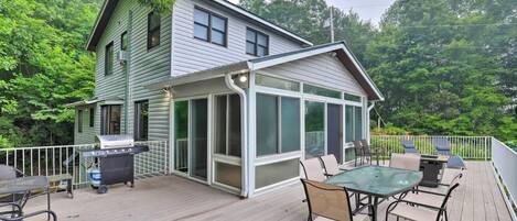 A house with a covered patio area featuring a table and chairs, a grill, and a trash can.