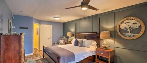 A bedroom with a bed, bedside tables, a ceiling fan, a wall-mounted lamp, and a decorative tree artwork.