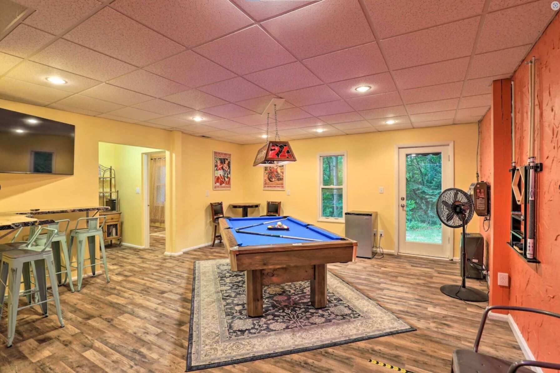Une table de billard dans une pièce au plancher en bois, avec un ventilateur au plafond et une porte donnant sur l’extérieur.