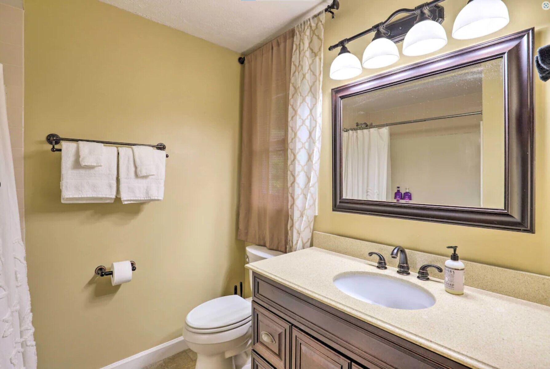 A bathroom with a sink, mirror, and toilet. There are towels hanging on a rack and a shower curtain.